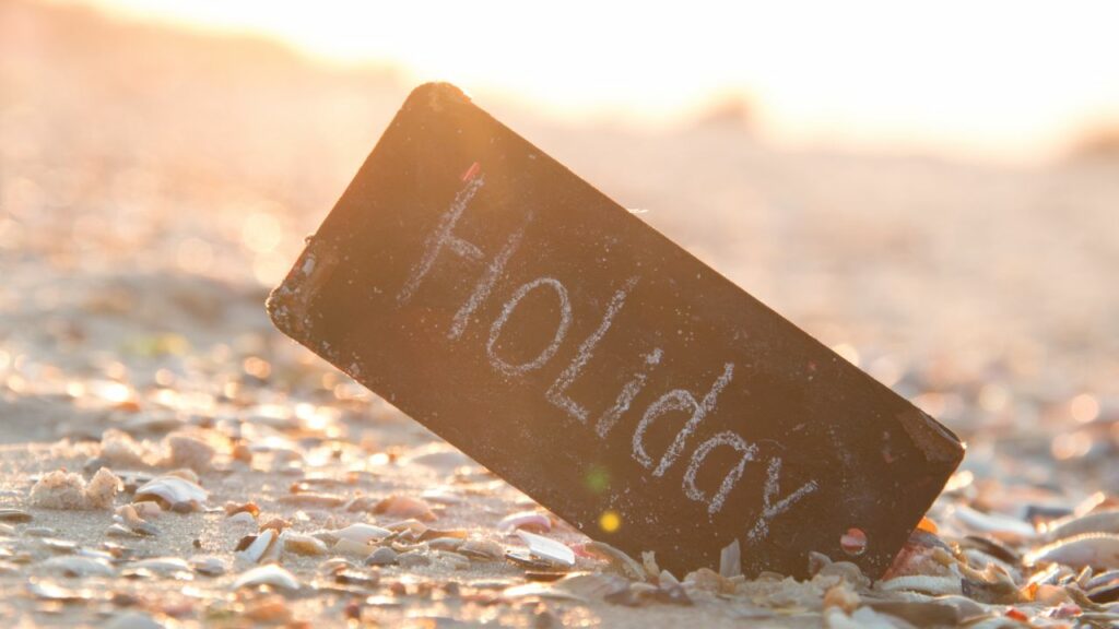 Strand mit Muscheln und einem Schild auf dem Holiday steht - Streit im Urlaub - Tipps für einen erholsamen Urlaub als Paar